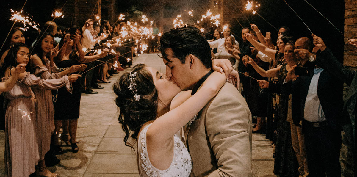 Image of a bride and groom kissing at a large wedding party in a lavish hall